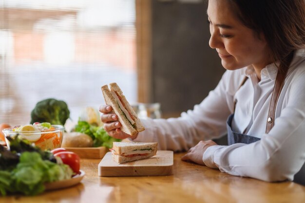 Imagem de close de uma bela chef cozinhando e comendo um sanduíche de trigo integral na cozinha