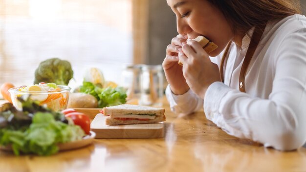 Imagem de close de uma chef feminina cozinhando e comendo um sanduíche de trigo integral na cozinha