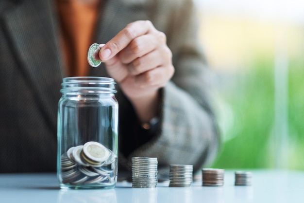 Imagem de close de uma empresária coletando e colocando moedas em uma jarra de vidro