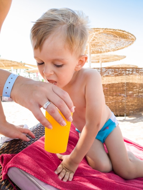 Imagem de close de uma jovem dando um copo de laranja para seu filho na praia