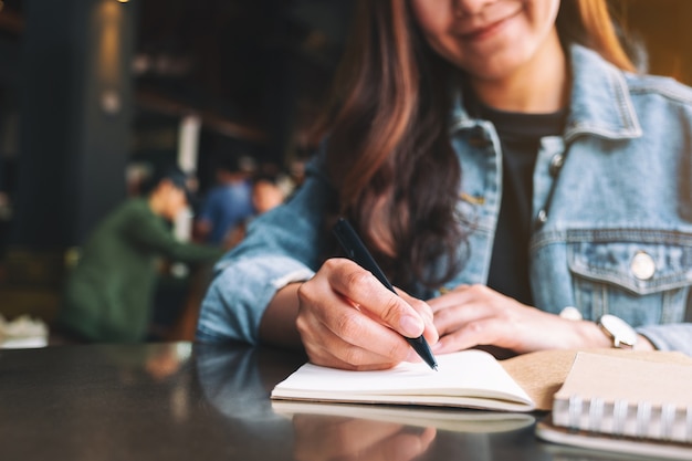 Imagem de close de uma linda mulher asiática escrevendo em um caderno em branco sobre a mesa