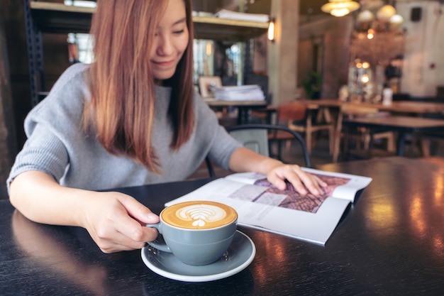 Imagem de close de uma linda mulher asiática lendo revista enquanto bebe café em um café moderno