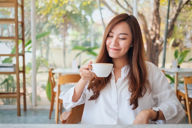 Imagem de close de uma linda mulher asiática segurando e bebendo café quente sentindo-se bem no café