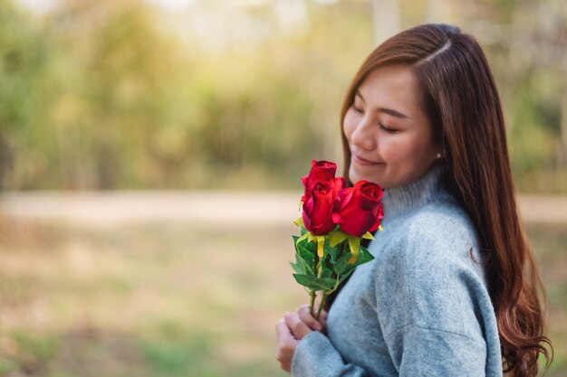 Imagem de close de uma linda mulher asiática segurando e cheirando flores de rosas vermelhas e se sentindo feliz no dia dos namorados