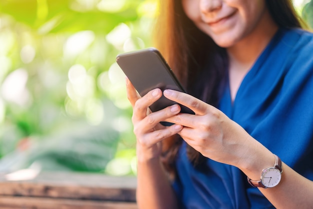 Imagem de close de uma linda mulher asiática segurando, usando e olhando para um telefone celular no jardim