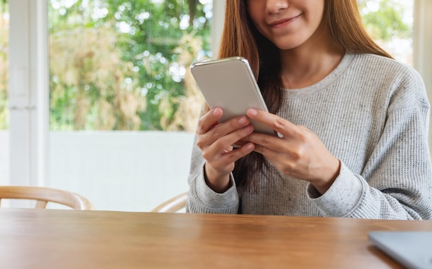 Imagem de close de uma linda mulher asiática segurando, usando e olhando para um telefone inteligente