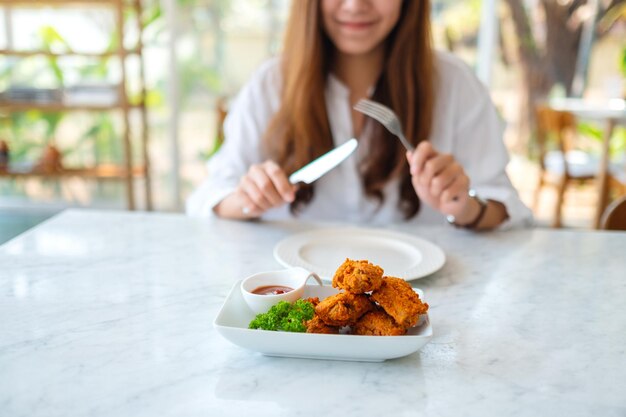 Imagem de close de uma linda mulher asiática usando garfo e faca para comer frango frito em um restaurante