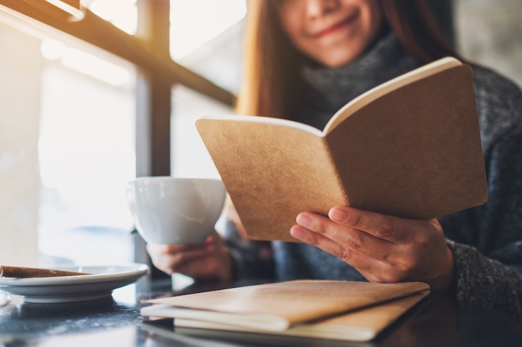 Foto imagem de close de uma linda mulher lendo um livro enquanto toma café pela manhã