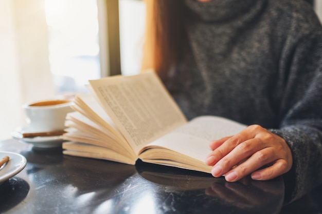 Imagem de close de uma linda mulher segurando e lendo um livro com uma xícara de café na mesa