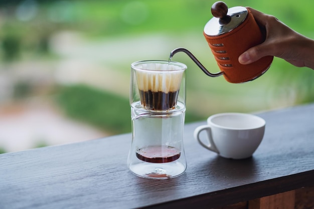 Imagem de close de uma mão despejando água quente de uma chaleira para fazer café com fundo borrado