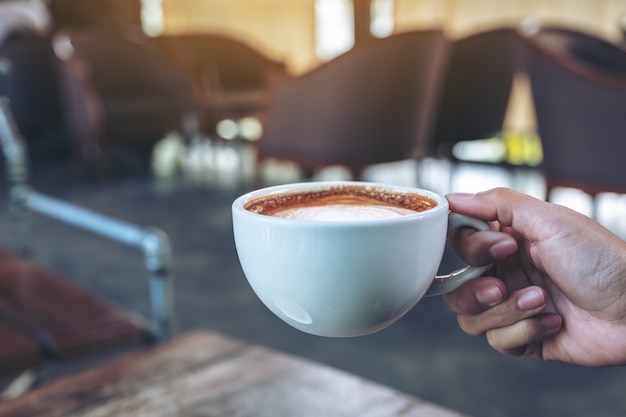 Imagem de close de uma mão segurando uma xícara azul de café quente na mesa de madeira no café