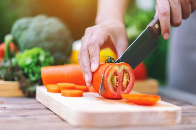 Imagem de close de uma mulher cortando e picando tomate com uma faca na placa de madeira