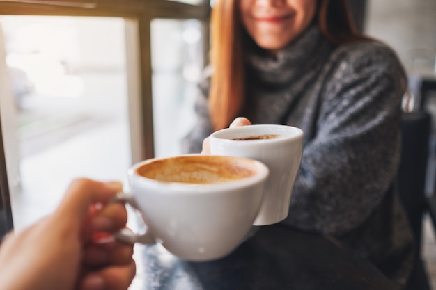 Imagem de close de uma mulher e um homem tilintando canecas de café em um café