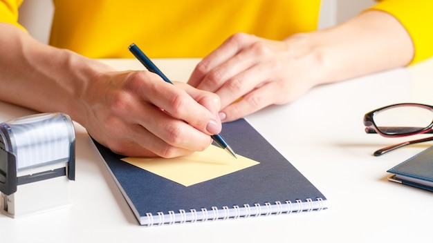 Imagem de close de uma mulher escrevendo em um cartão de papel amarelo