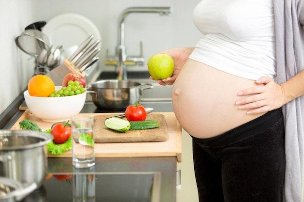 Imagem de close de uma mulher grávida fazendo o jantar na cozinha