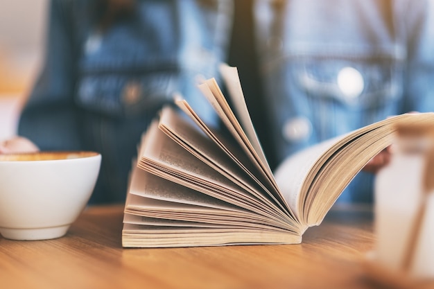 Imagem de close de uma mulher segurando e lendo um livro de romance vintage enquanto bebia café