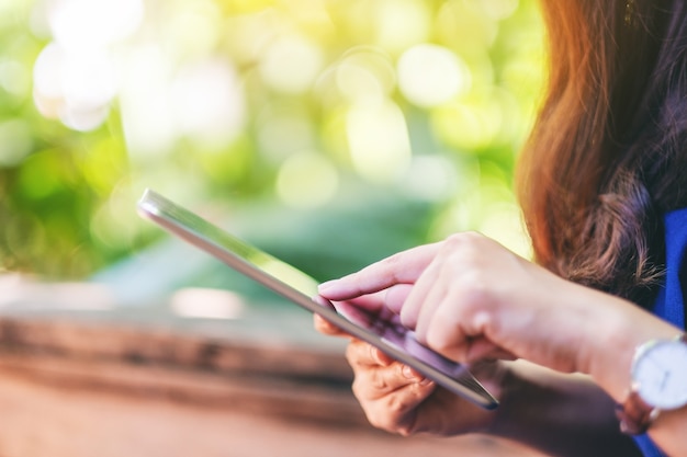 Imagem de close de uma mulher segurando e usando o tablet pc enquanto está sentada no jardim