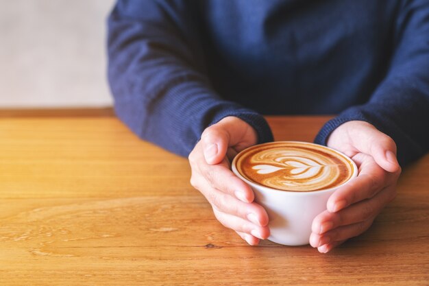 Imagem de close de uma mulher segurando uma xícara de café quente na mesa de madeira