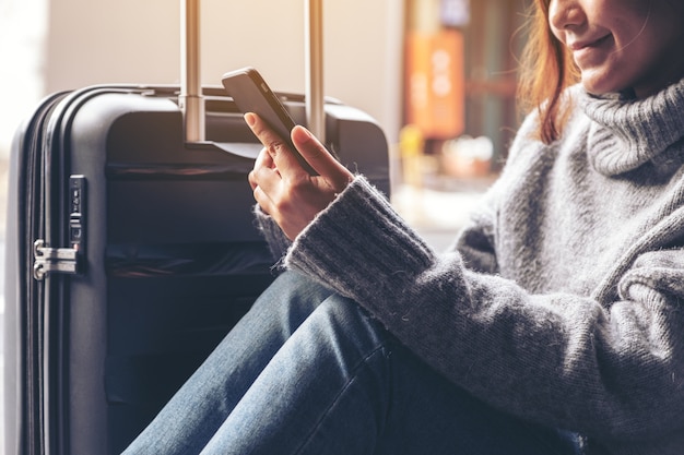 Imagem de close de uma mulher sentada usando um telefone celular com uma bagagem preta para viajar