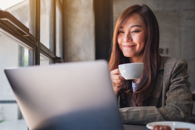 Imagem de close de uma mulher trabalhando e digitando em um laptop enquanto toma café em um café