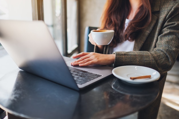 Imagem de close de uma mulher trabalhando e tocando no touchpad do laptop enquanto bebe café no escritório