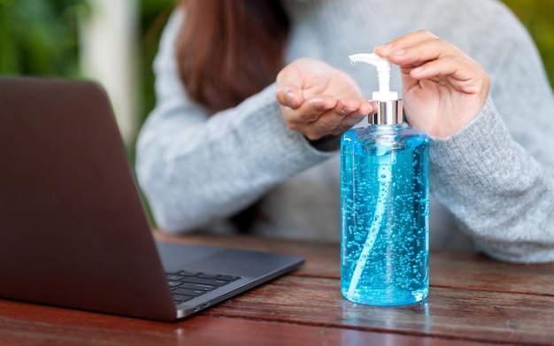 Imagem de close de uma mulher usando e aplicando álcool gel para limpar as mãos enquanto trabalhava no laptop em casa para o conceito de vírus Healthcare e Covid-19 ou 2020