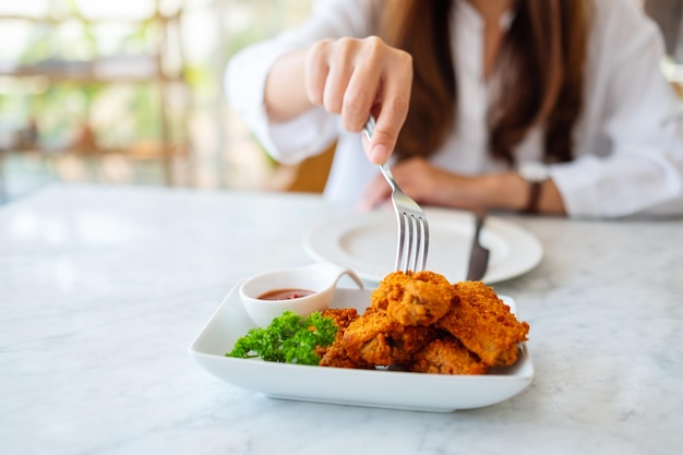 Imagem de close de uma mulher usando um garfo para comer frango frito em um restaurante