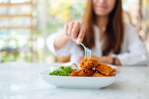Imagem de close de uma mulher usando um garfo para comer frango frito em um restaurante