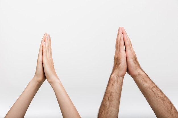 Foto imagem de close up das mãos levantadas de um homem e de uma mulher isoladas sobre a parede branca, mostrando por favor, reze o gesto.