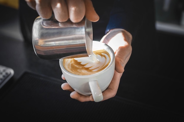 Imagem de close-up de mãos masculinas derramando leite e preparando cappuccino fresco, artista de café e conceito de preparação, café da manhã