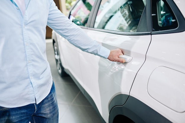 Imagem de close-up de um homem abrindo a porta traseira de um carro novo