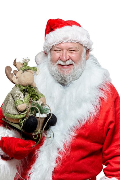 Imagem de close up de um papai noel feliz em um casaco vermelho, luvas e um chapéu, segurando um brinquedo nas mãos, apontando o dedo indicador, isolado em um fundo branco.