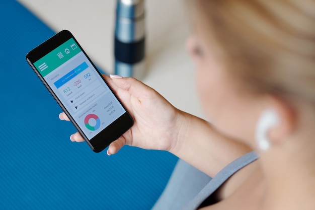 Imagem de close-up de uma jovem verificando sua atividade por meio de um aplicativo móvel em um smartphone após o treino em casa