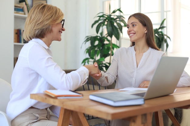 Imagem de colegas discutindo documentos e apertando as mãos.