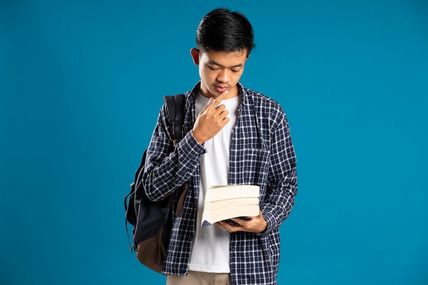 Imagem de conteúdo do estudante do sexo masculino pensando de bruços enquanto olha para o livro isolado em fundo azul