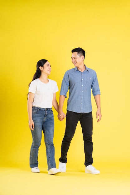 Imagem de corpo inteiro de casal asiático posando em fundo amarelo