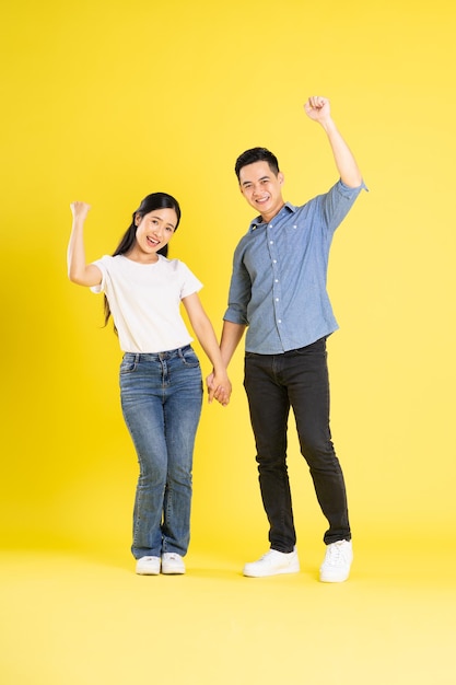 Imagem de corpo inteiro de casal asiático posando em fundo amarelo