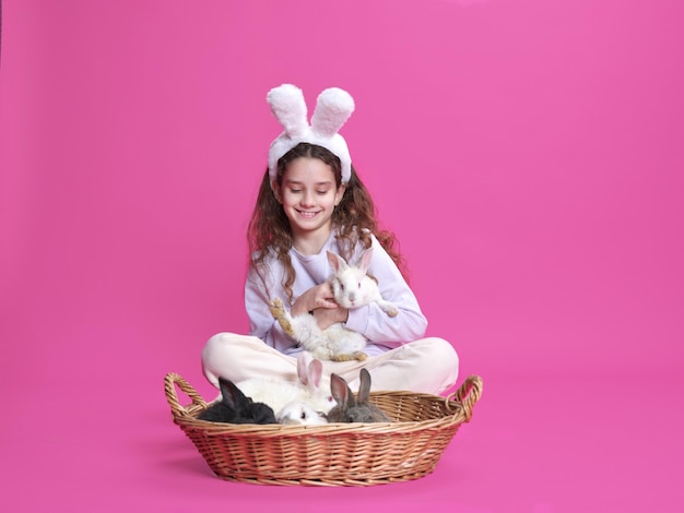 Imagem de corpo inteiro de uma menina com orelhas de coelho branco segurando um coelho nas mãos isoladas em um fundo rosa