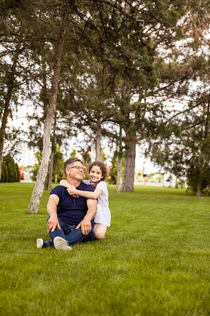 Imagem de corpo inteiro de uma sobrinha abraça o avô no parque em um dia ensolarado. Retrato ao ar livre. Conceito de família.
