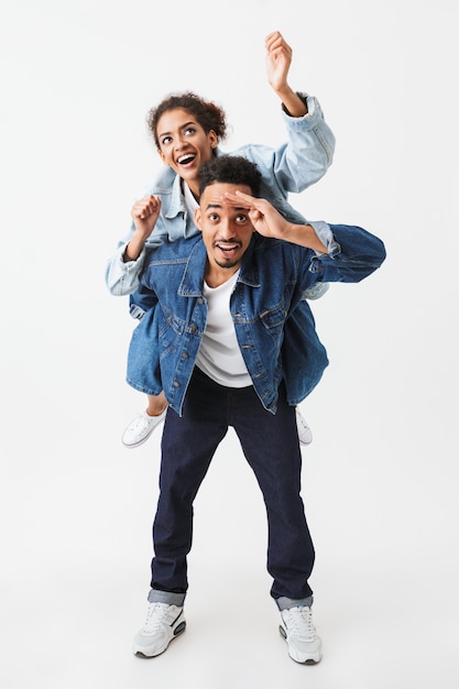 Imagem de corpo inteiro do feliz casal Africano em camisas jeans se divertindo juntos sobre parede cinza