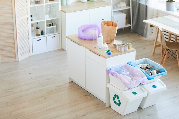 Imagem de cozinha doméstica com lixo na mesa, classificado em sacos de papel ecológico e lixeiras