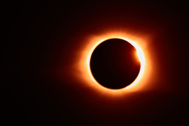 Imagem de eclipse solar com erupção solar que cria um brilho laranja ao redor da lua negra