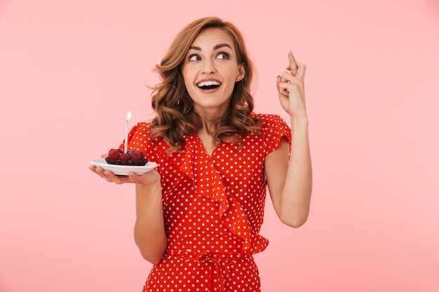 Foto imagem de emocional jovem feliz posar isolado sobre a parede rosa, segurando o bolo de aniversário, esperançoso, por favor, faça um desejo.