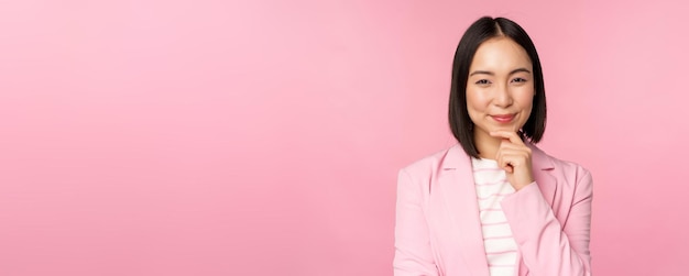 Imagem de empresária asiática em pé em pose de pensamento usando terno empresário de vendedora coreana posando contra fundo rosa