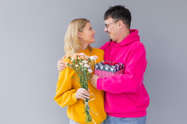 Imagem de feliz casal amoroso isolado segurando flores e caixa de presente de presente