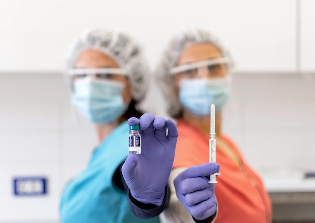 Imagem de foco seletivo de duas enfermeiras usando máscaras protetoras, segurando vacina e seringa, covid.
