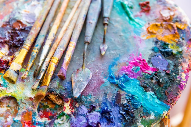 Imagem de fundo de tintas de cores misturadas brilhantes na paleta de arte com pincéis e facas de paleta