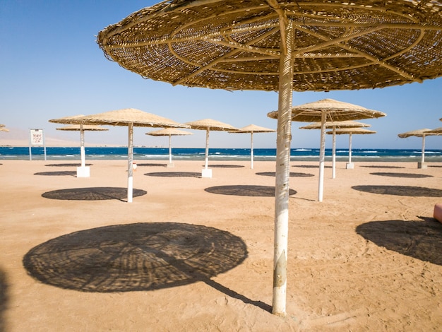 Imagem de guarda-sóis de palha na praia do oceano em um dia quente de sol contra o céu azul