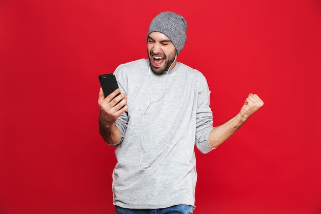 Imagem de homem alegre de 30 anos ouvindo música com fone de ouvido e celular, isolada