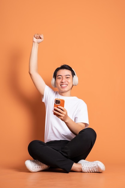 Imagem de homem asiático sentado usando telefone e isolado em fundo laranja